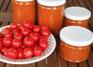 Frische Tomaten auf einem Teller. Daneben Schraubdeckelgläser mit Tomatensoße. 